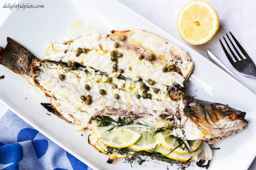 Grilled whole branzino with lemon caper sauce on a serving plate