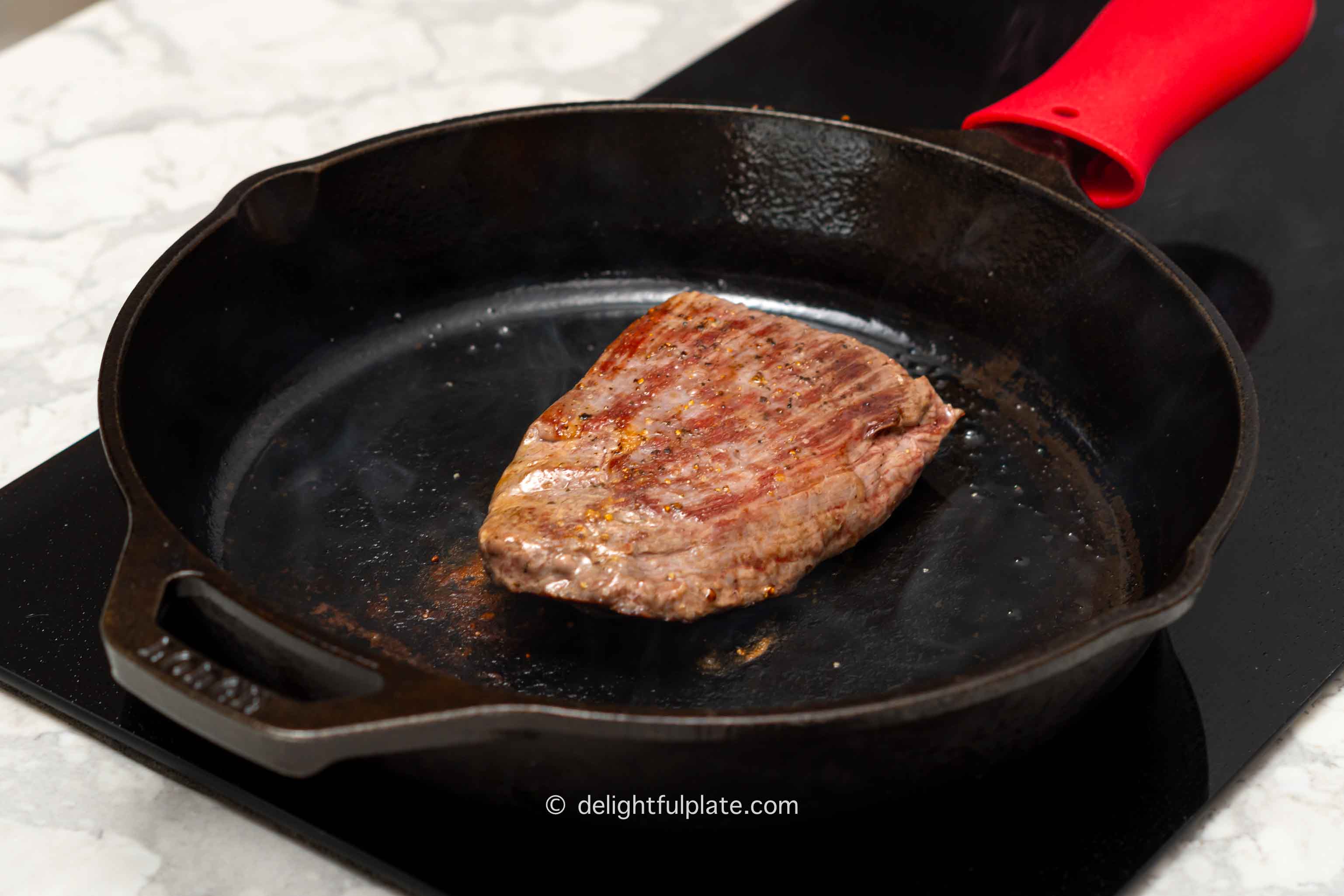 flank steak being seared in a cast iron skillet.