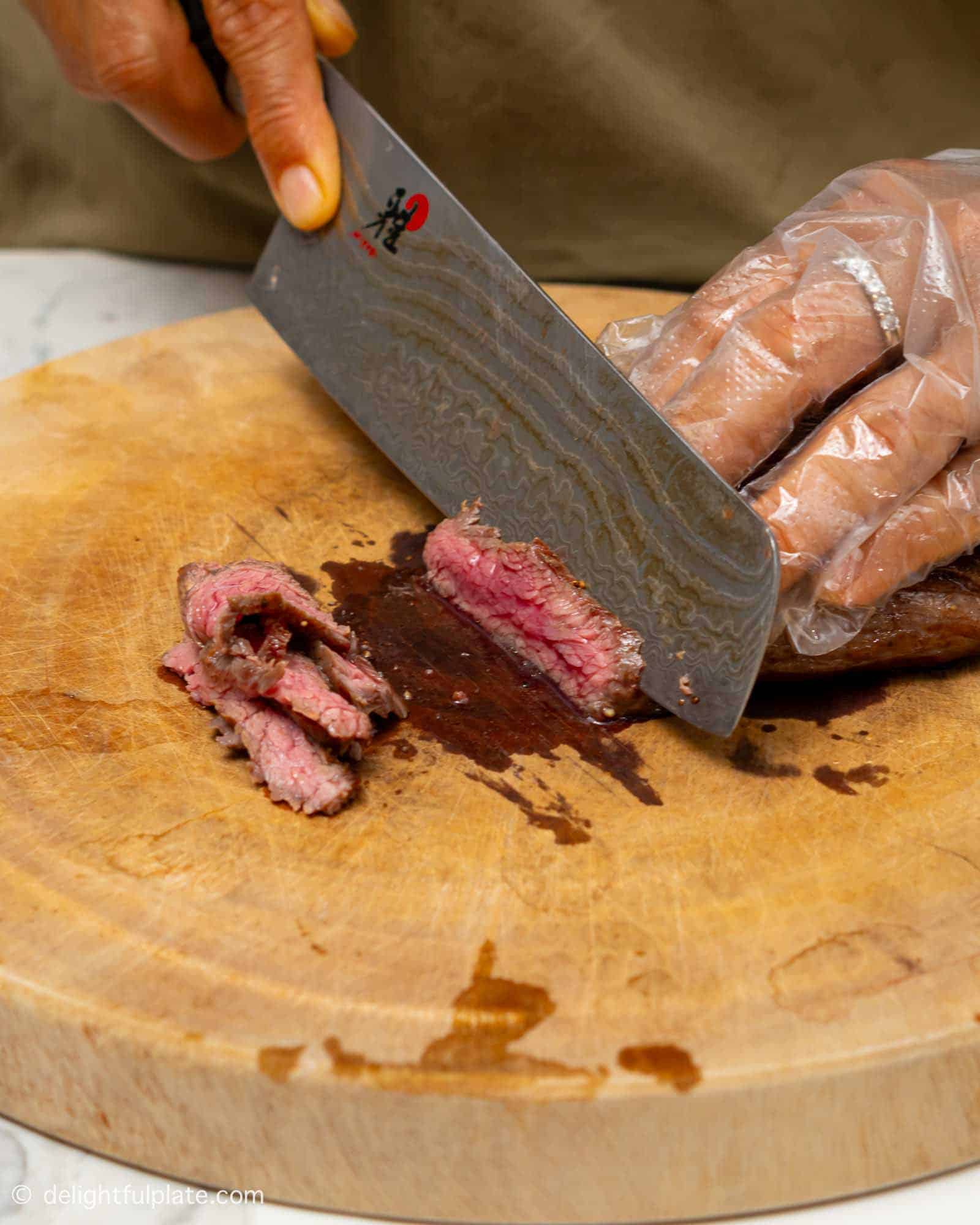 flank steak being sliced thinly on a cutting board.