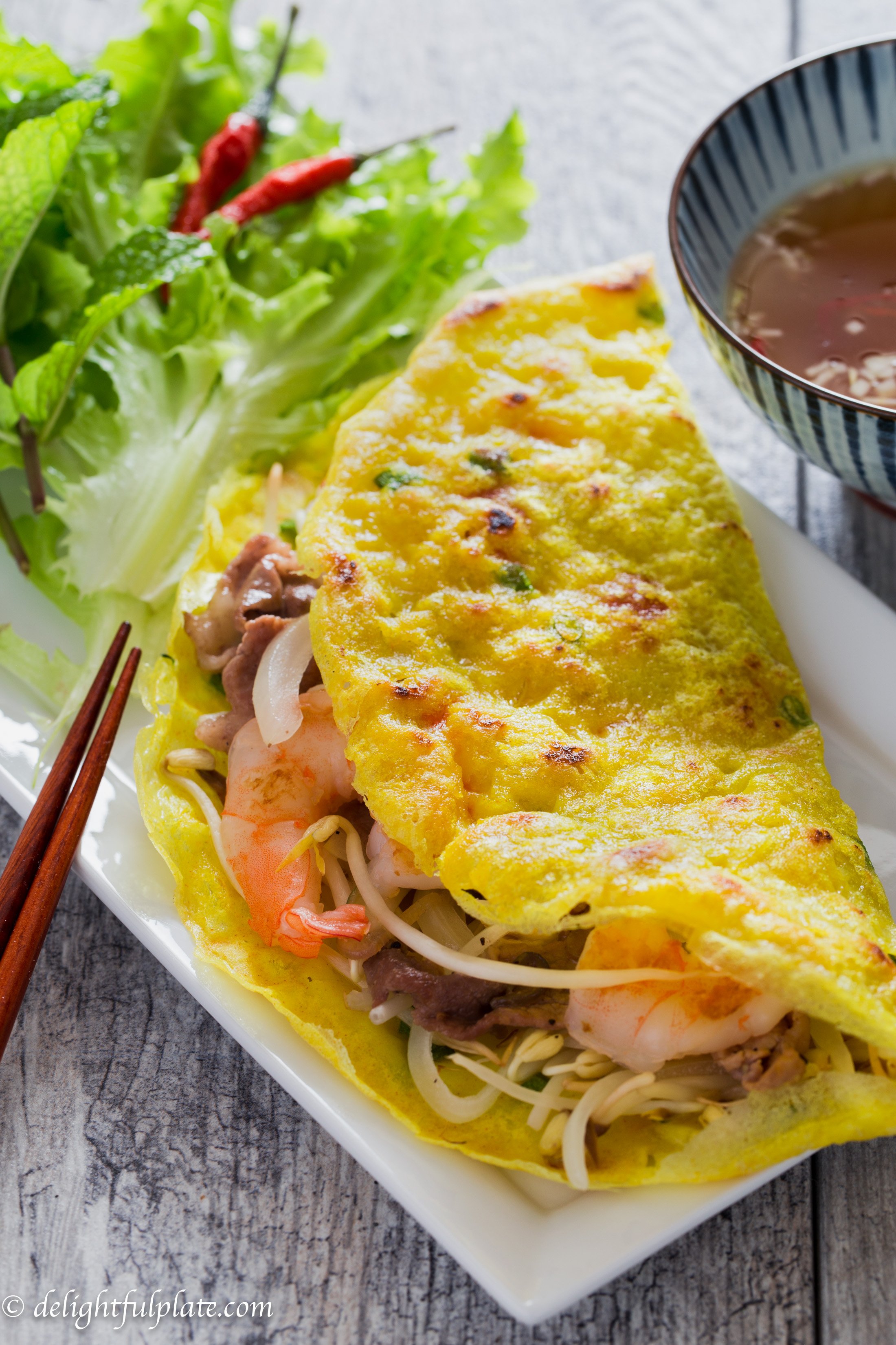 Vietnamese Crepe (Banh Xeo) on a serving plate with fresh herbs and refreshing dipping sauce