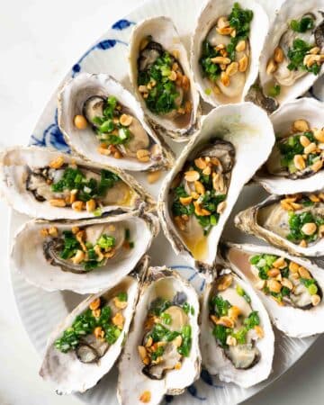 a plate of grilled oysters topped with scallion oil and roasted peanuts