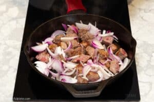 seared beef cubes and onion slices in the pan.