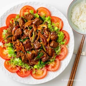 a plate of Vietnamese shaking beef placed on a bed of greens and tomato slices.
