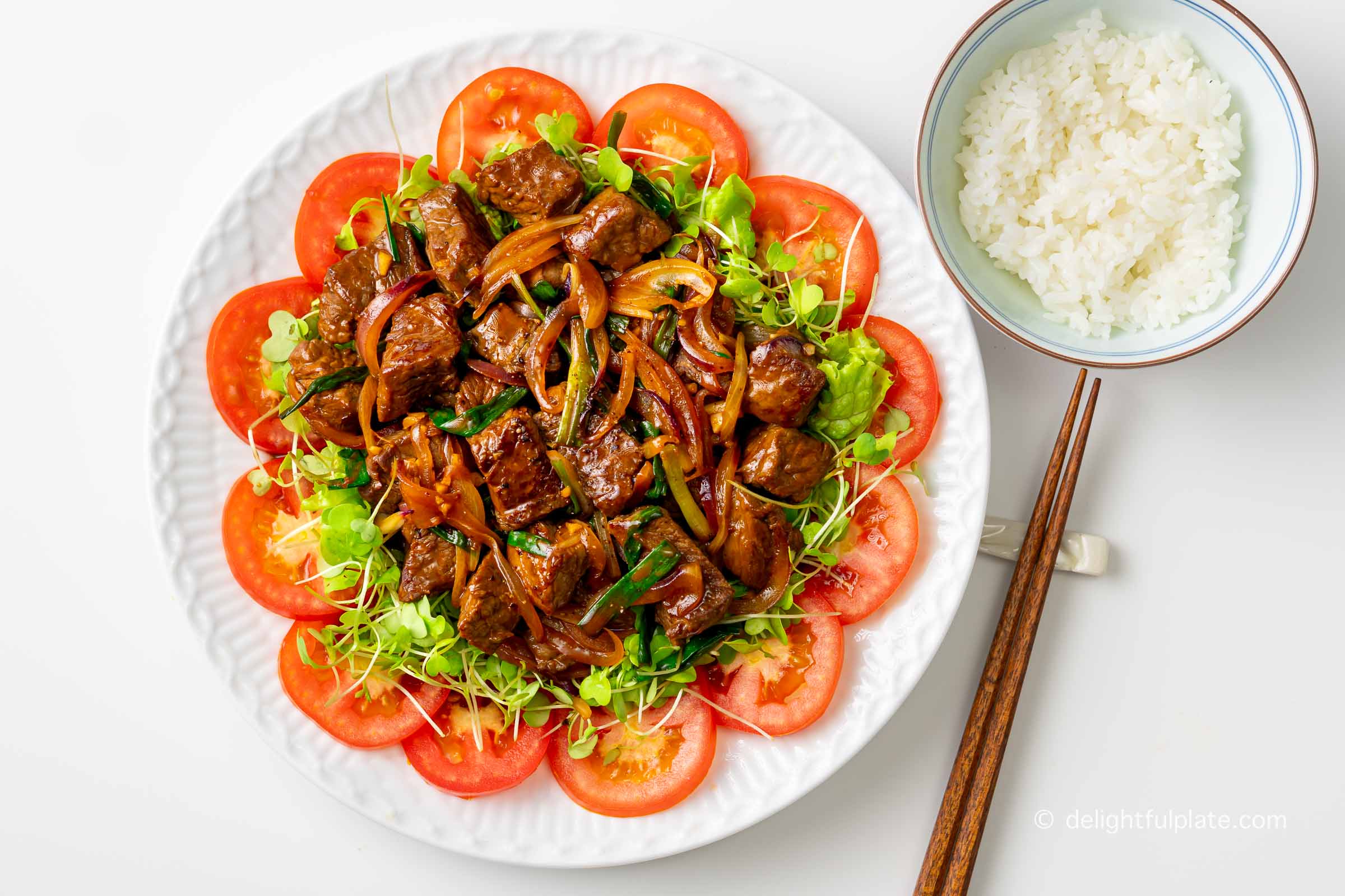 a plate of Vietnamese shaking beef (bo luc lac) with a bowl of rice on the side.