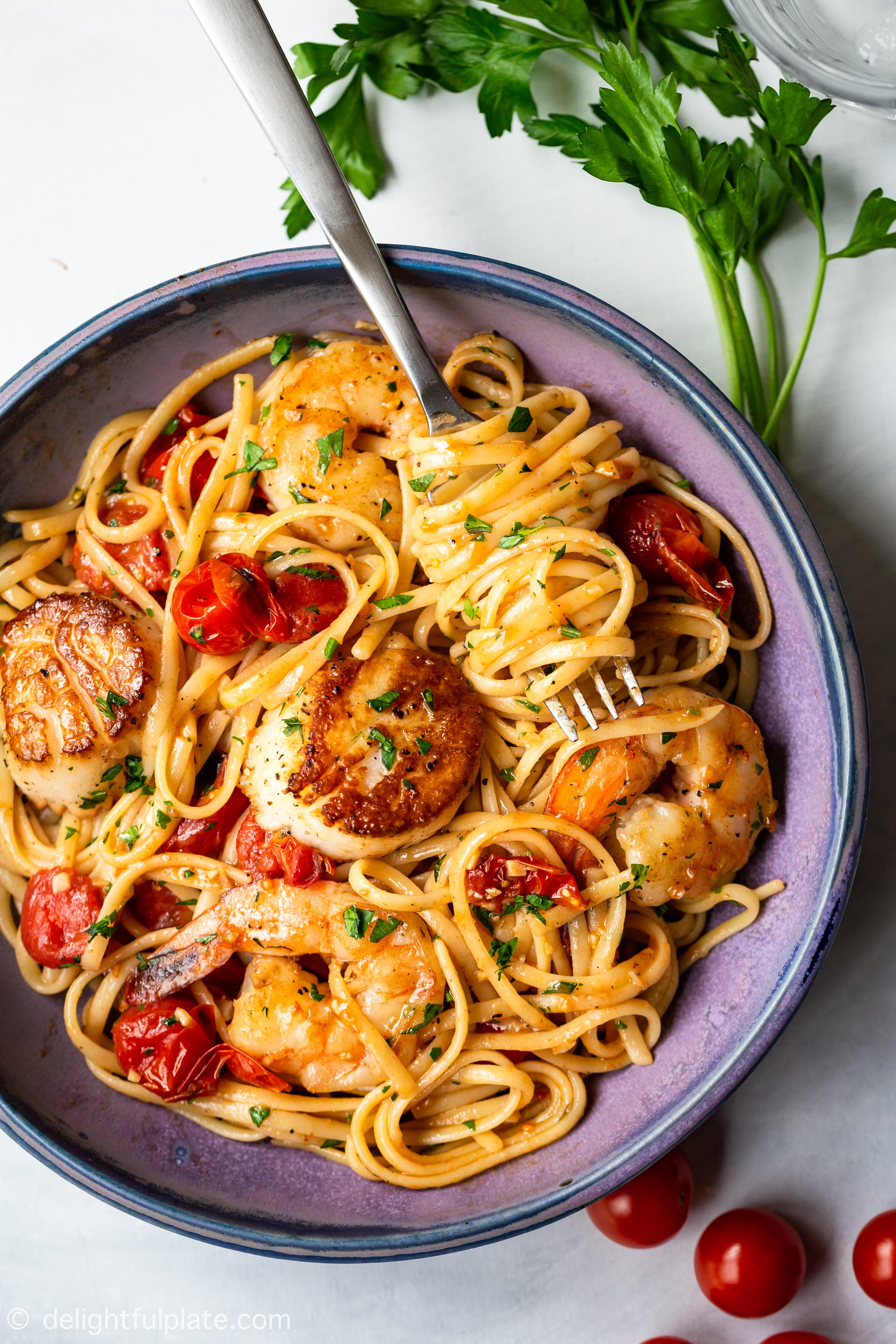 a plate of scallop shrimp pasta with burst cherry tomatoes