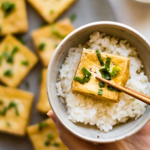 A crispy slice of tofu that has been dipped in scallion fish sauce, served over rice