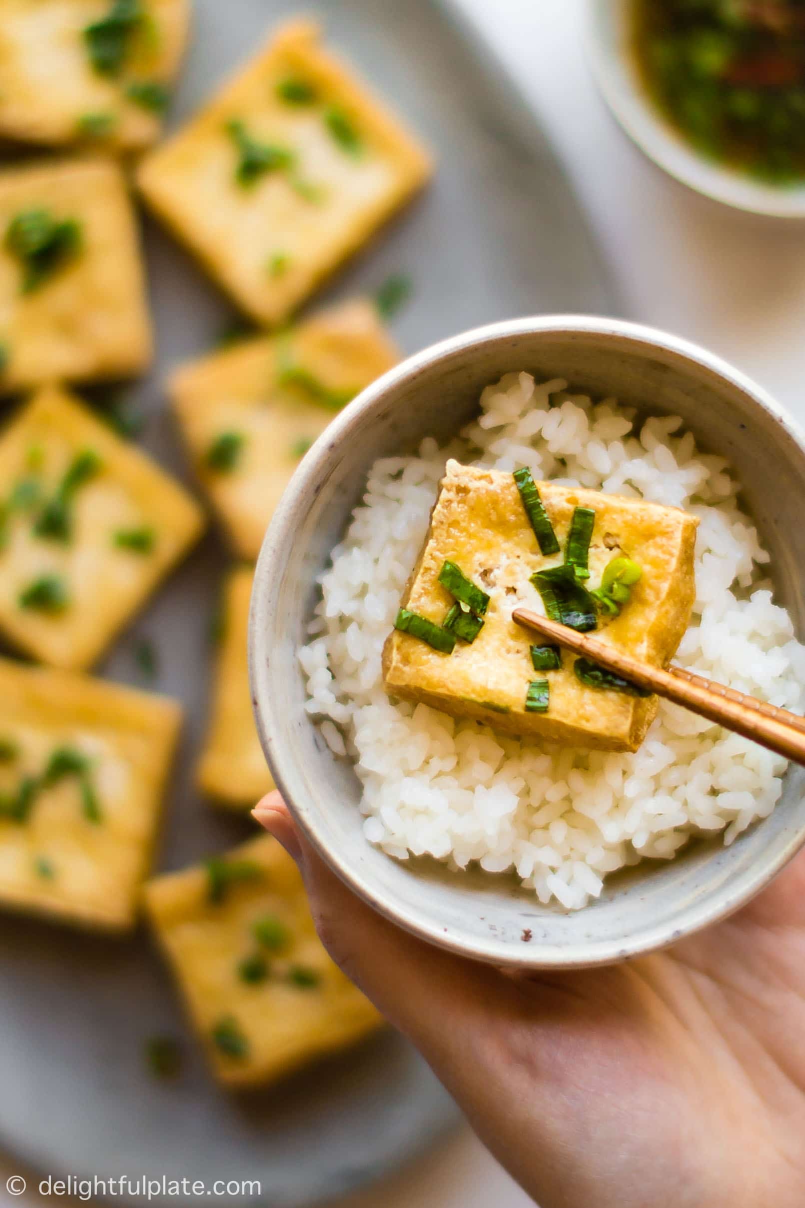A crispy slice of tofu that has been dipped in scallion fish sauce, served over rice