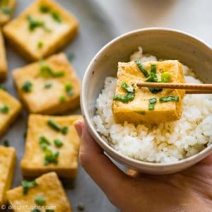 A crispy slice of tofu that has been dipped in scallion fish sauce, served with rice