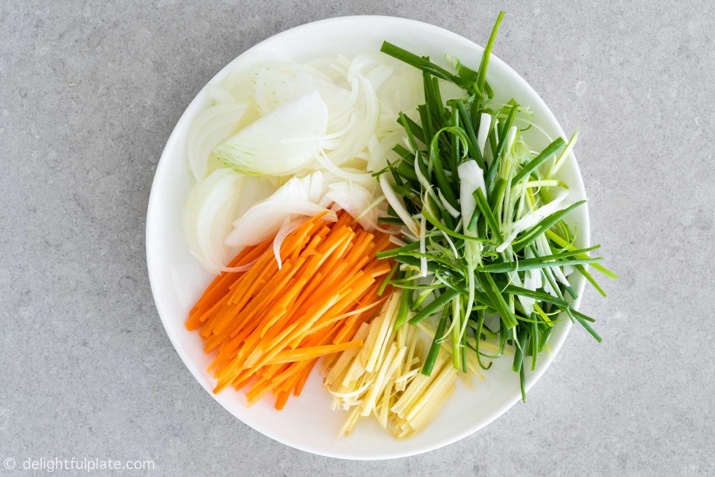 a plate with julienned ginger, carrots, scallions and onion