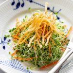 a plate of microgreens salad topped with crispy fried enoki mushrooms