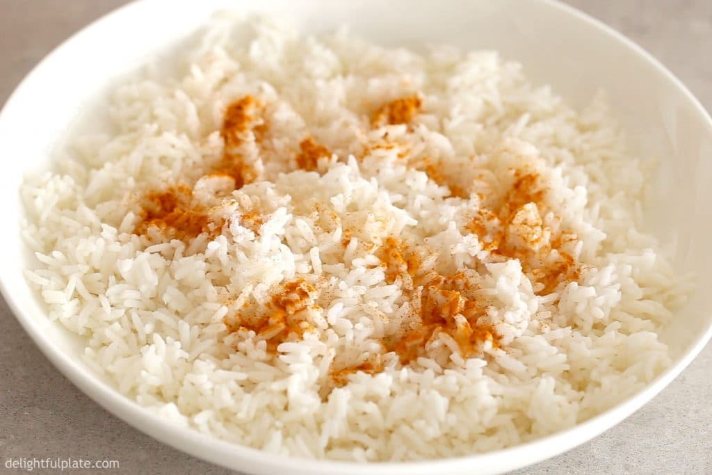 a plate with rice being mixed with turmeric powder