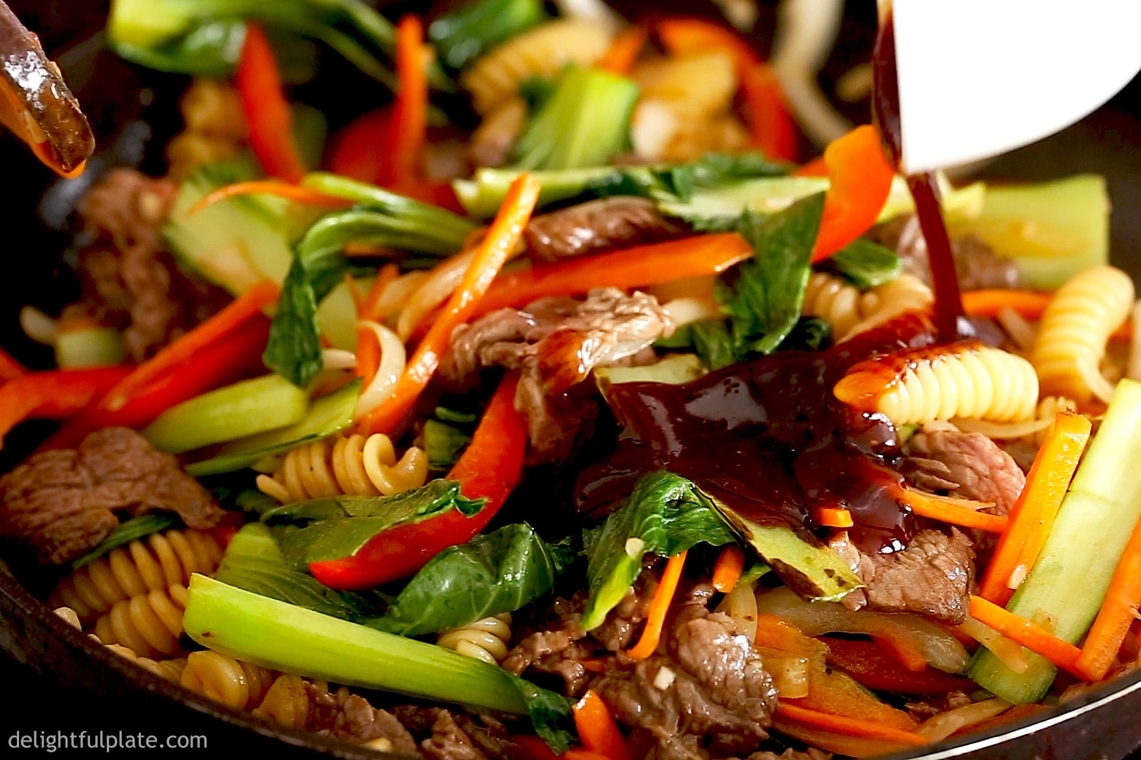 adding stir-fry sauce to beef, pasta and veggies in Vietnamese-style pasta dish.