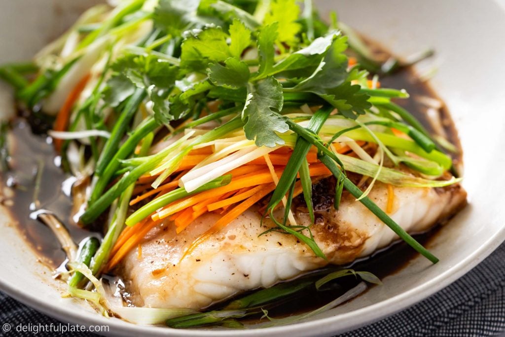 A plate of steamed fish with soy sauce, julienned ginger, scallions, onion and carrots