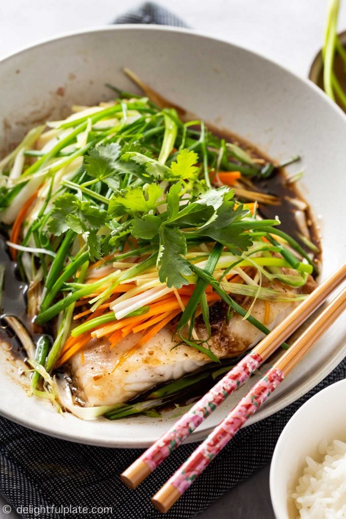 a plate of steamed fish with soy sauce, ginger, scallion, onion and carrot. Serve with rice