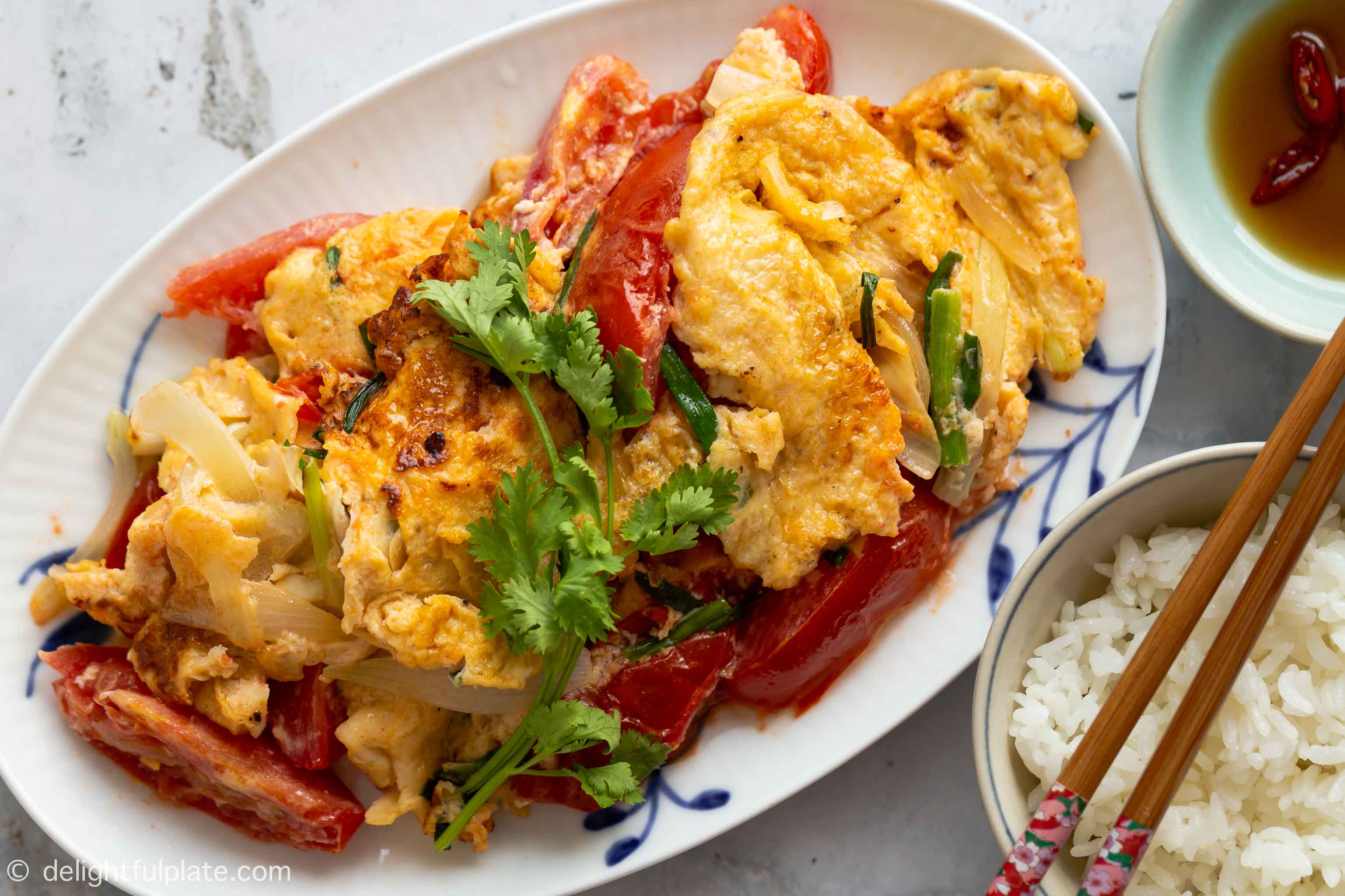 Omelet with tomatoes and onions being served with rice and fish sauce on the side