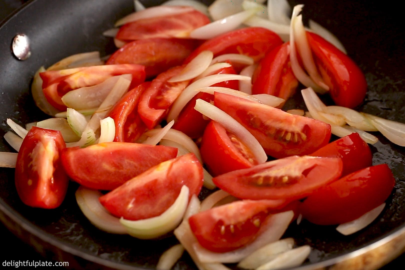 tomato wedges and onions are being sautéed in a skillet