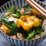a bowl with grilled fish marinated with turmeric on top of noodles, dills and scallions
