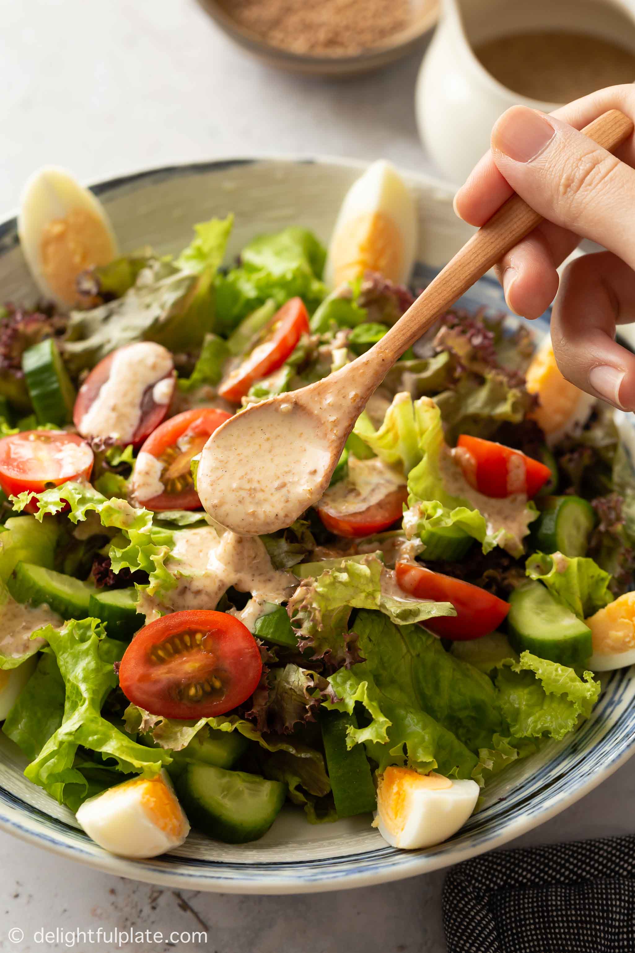 a plate of green salad with sesame dressing being drizzled on top