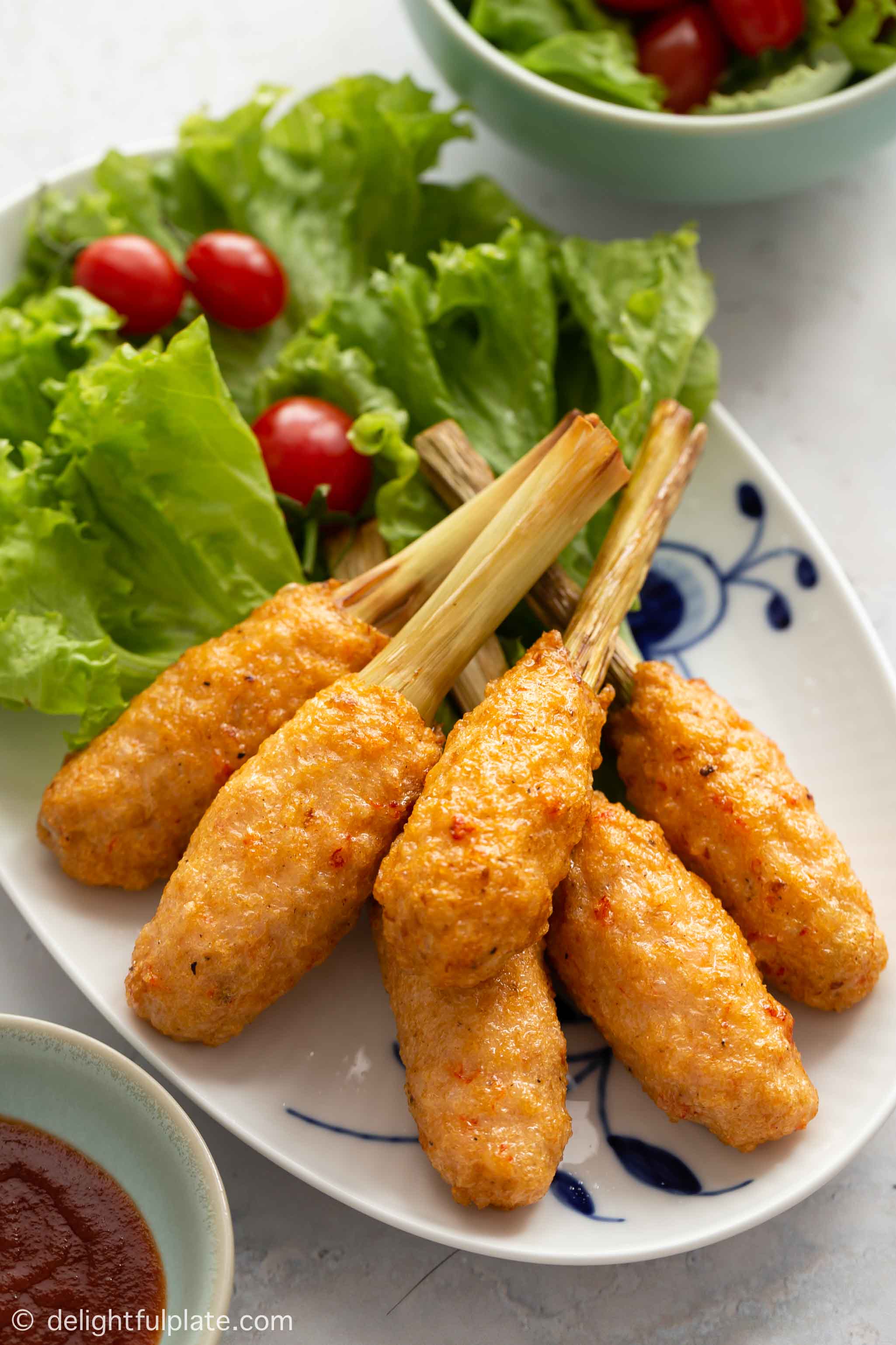 Golden Vietnamese shrimp sticks (Chao tom) on a serving plate with lettuce and cherry tomato