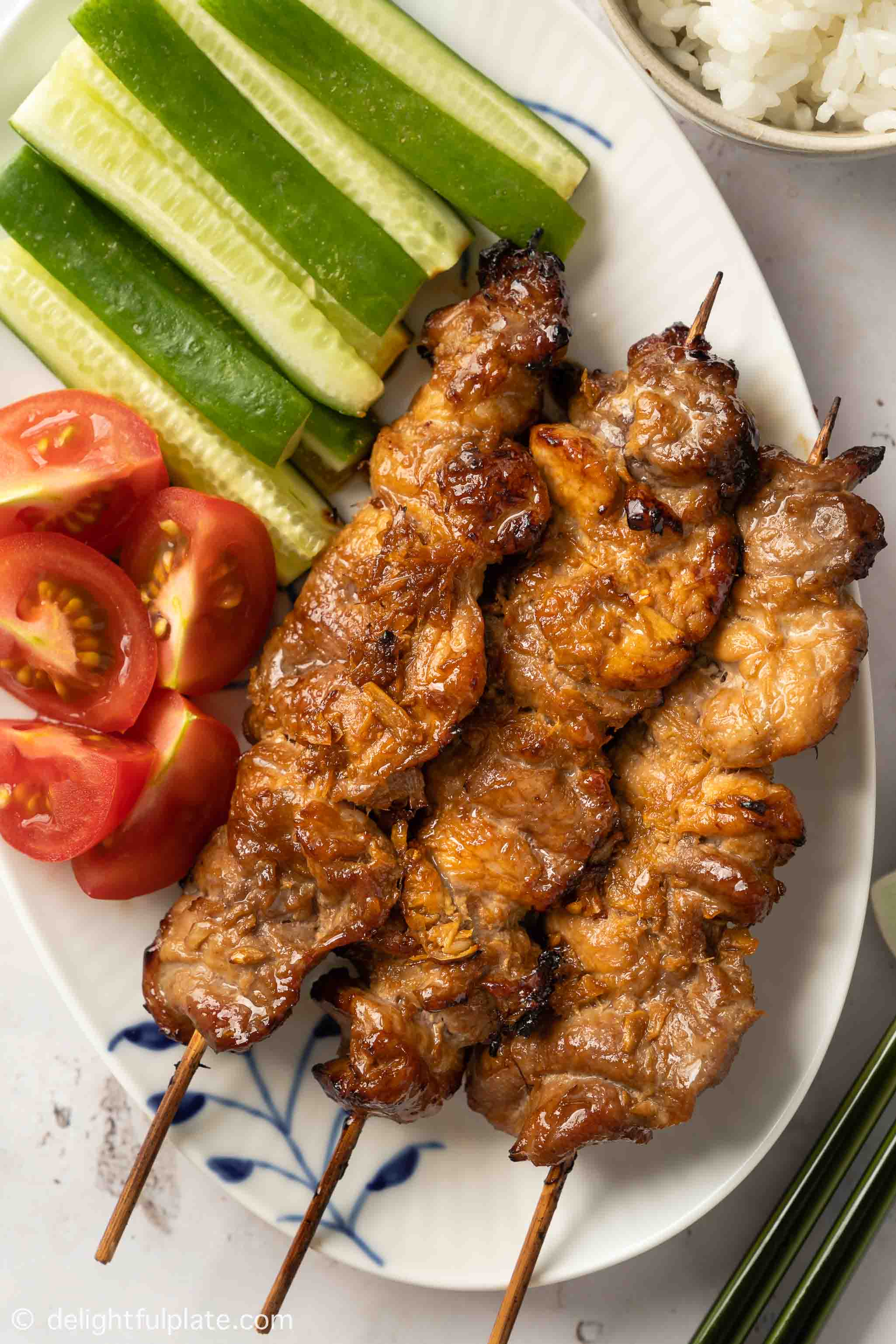 Asian pork skewers on a plate, served with cucumber and rice