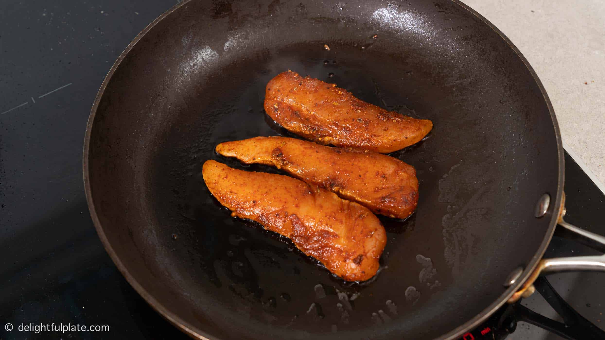 searing marinated chicken tenderloin in a skillet.