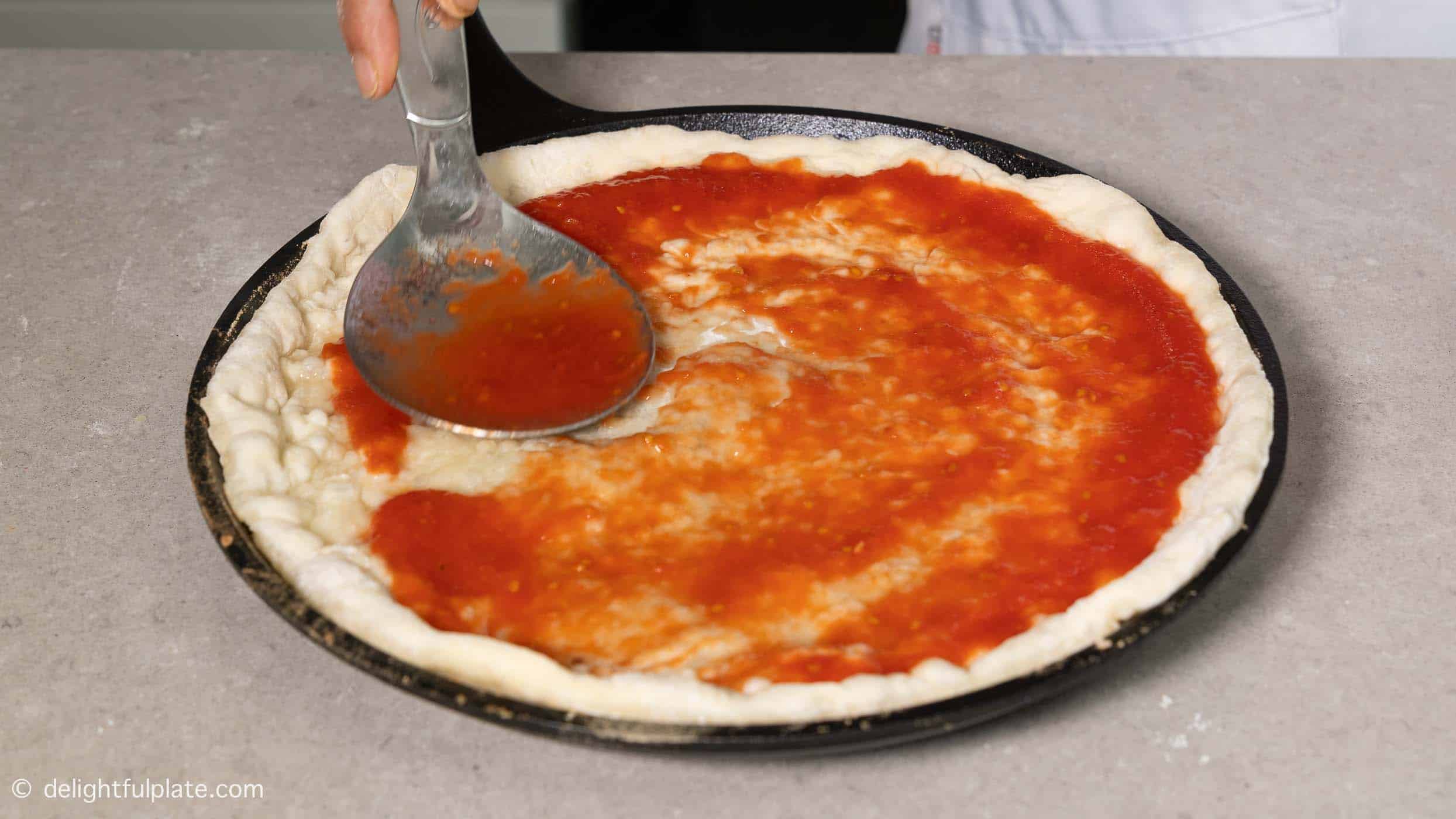 spreading tomato sauce on pizza crust.