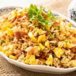 a plate of fried rice with bacon, eggs, carrots and onions