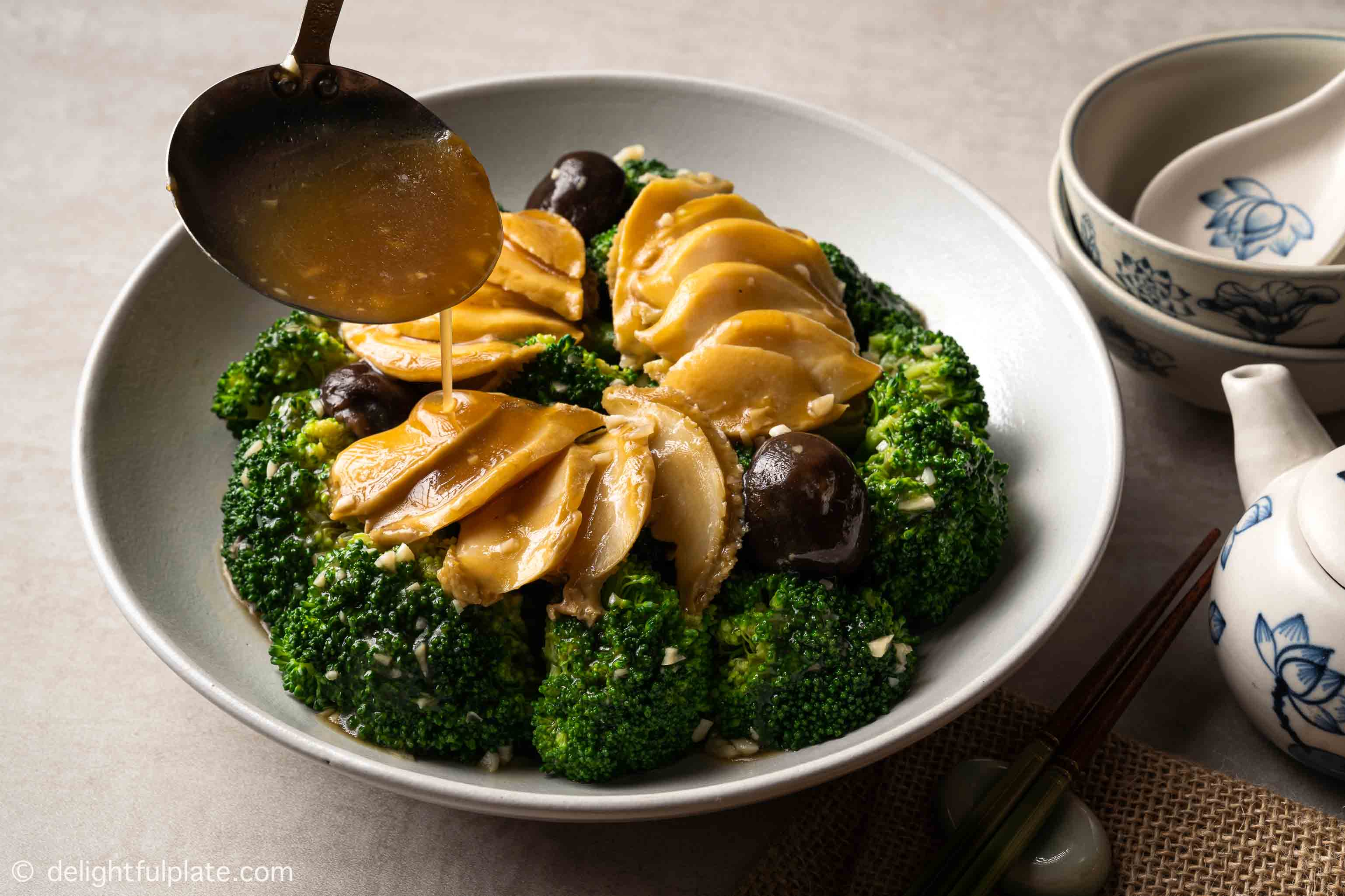 pouring oyster sauce over braised abalones and broccoli