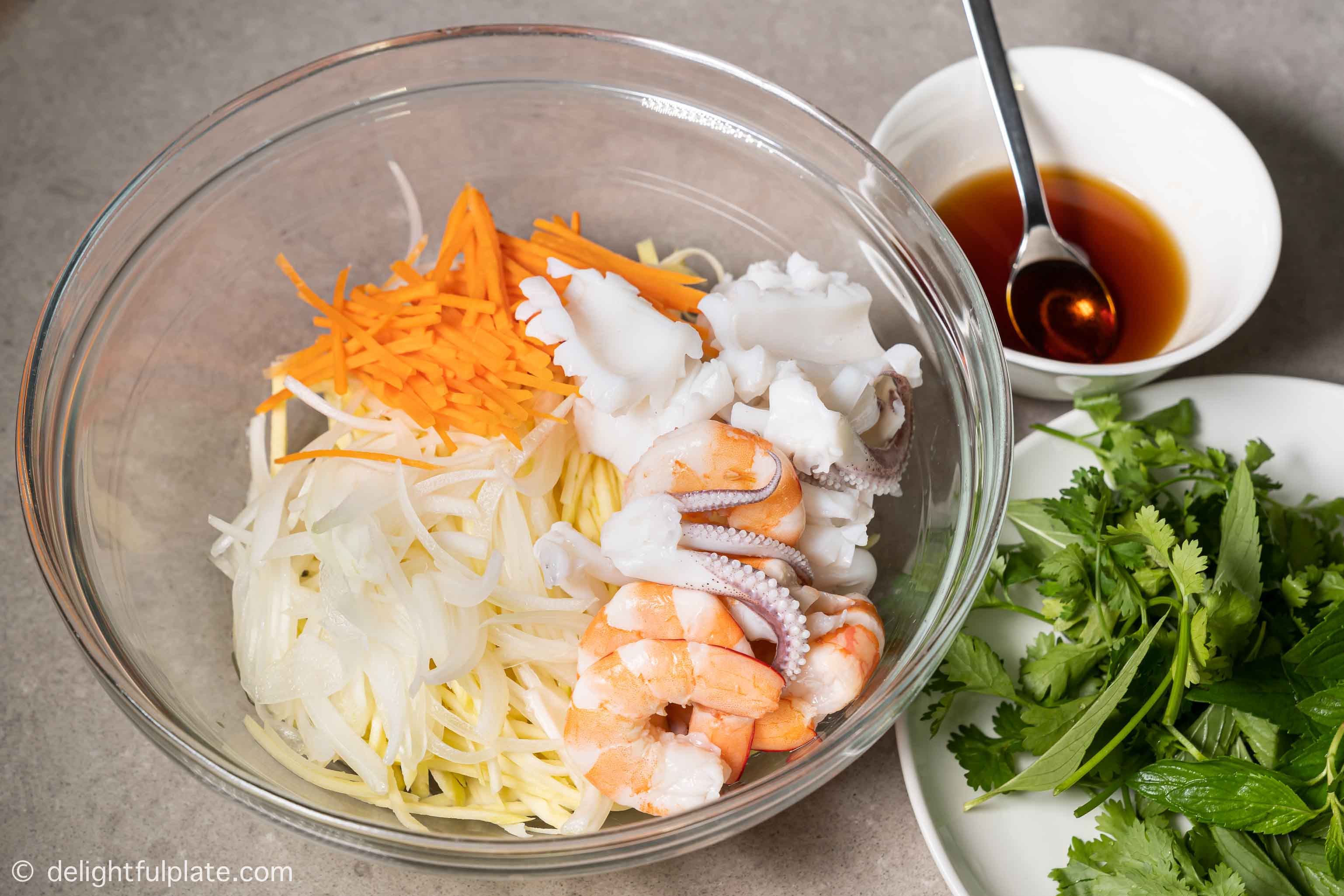 a mixing bowl with green mango, carrot, onion, shrimp and squid