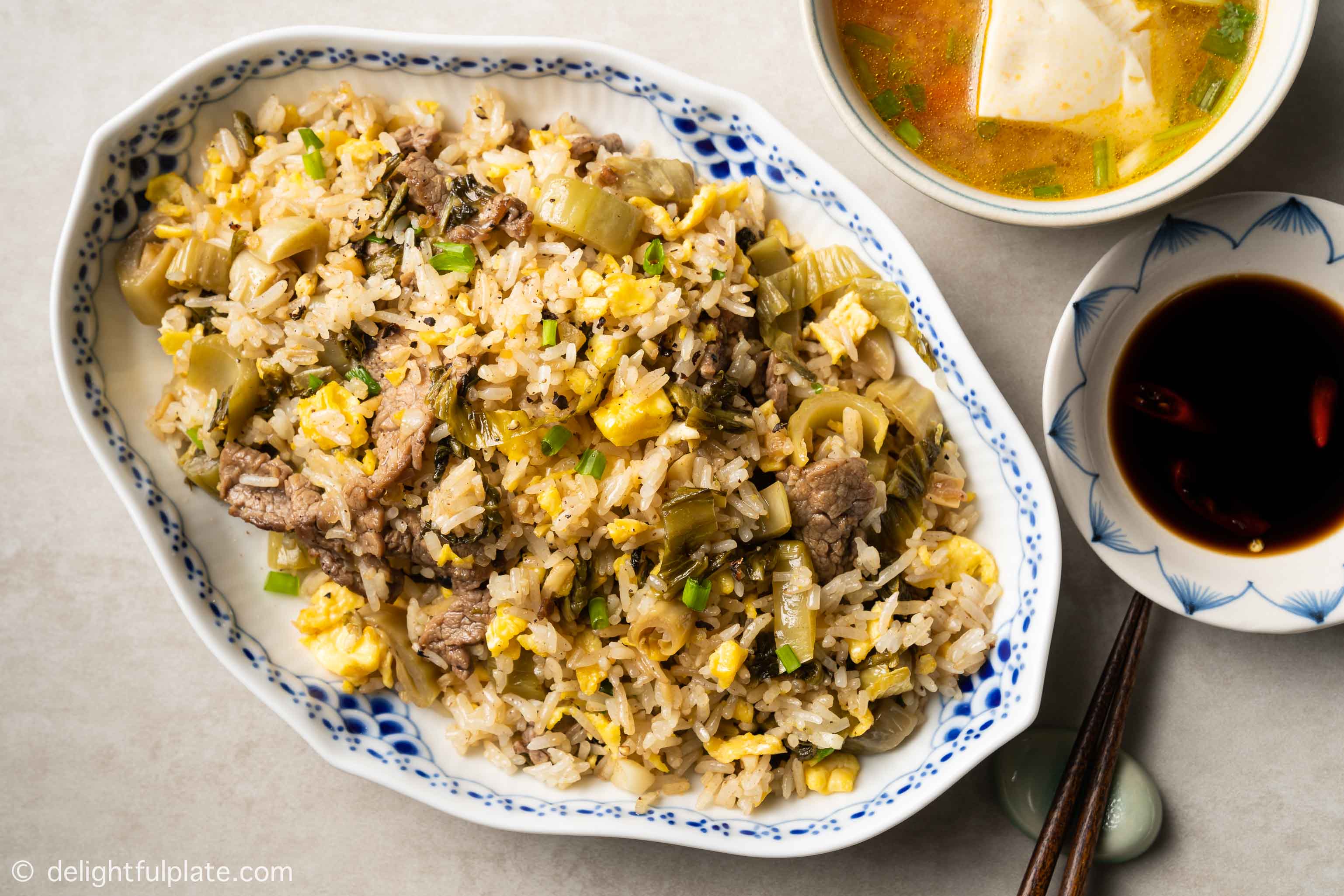 a plate of Vietnamese beef fried rice served with soy sauce and soup on the side