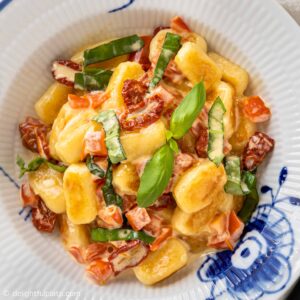a plate of creamy gnocchi with sun dried tomatoes and basil
