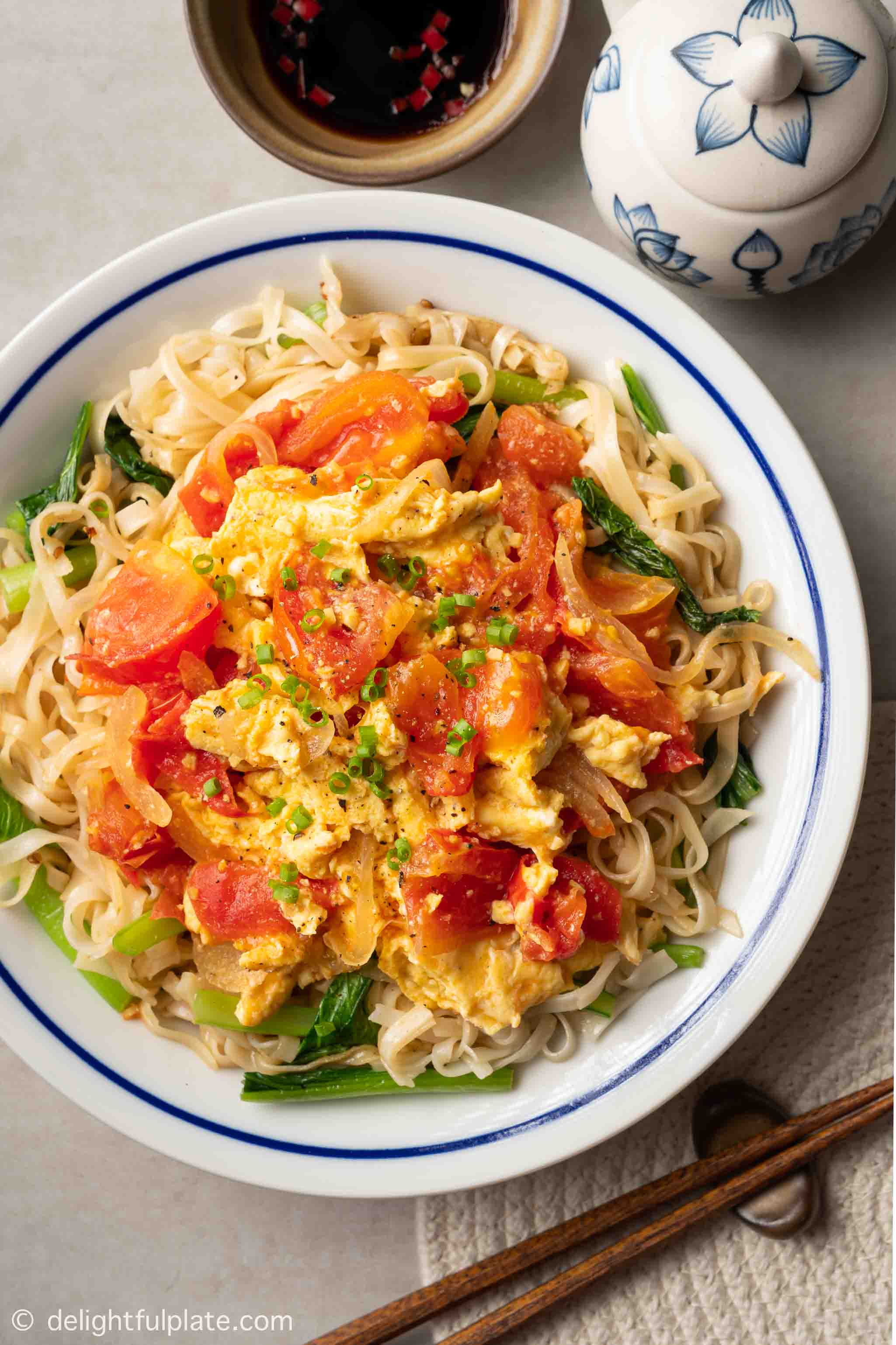 a plate of scrambled eggs with tomatoes and noodles