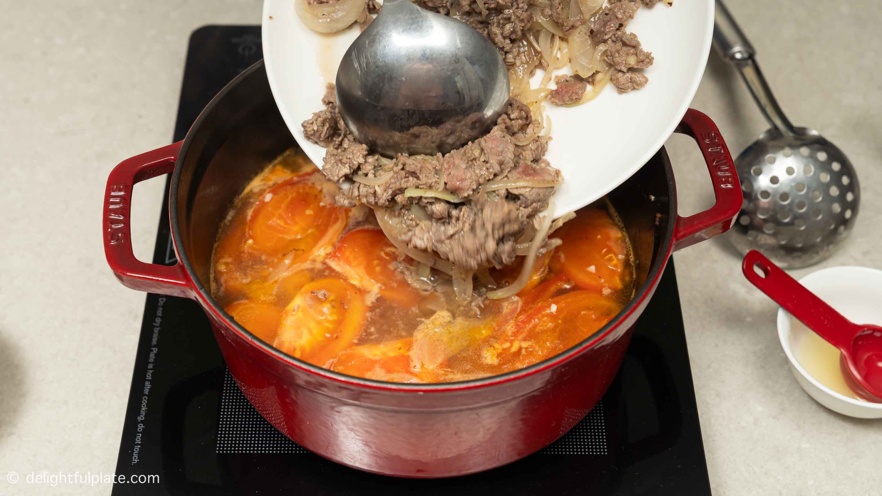 adding sautéed beef from a plate to the soup.