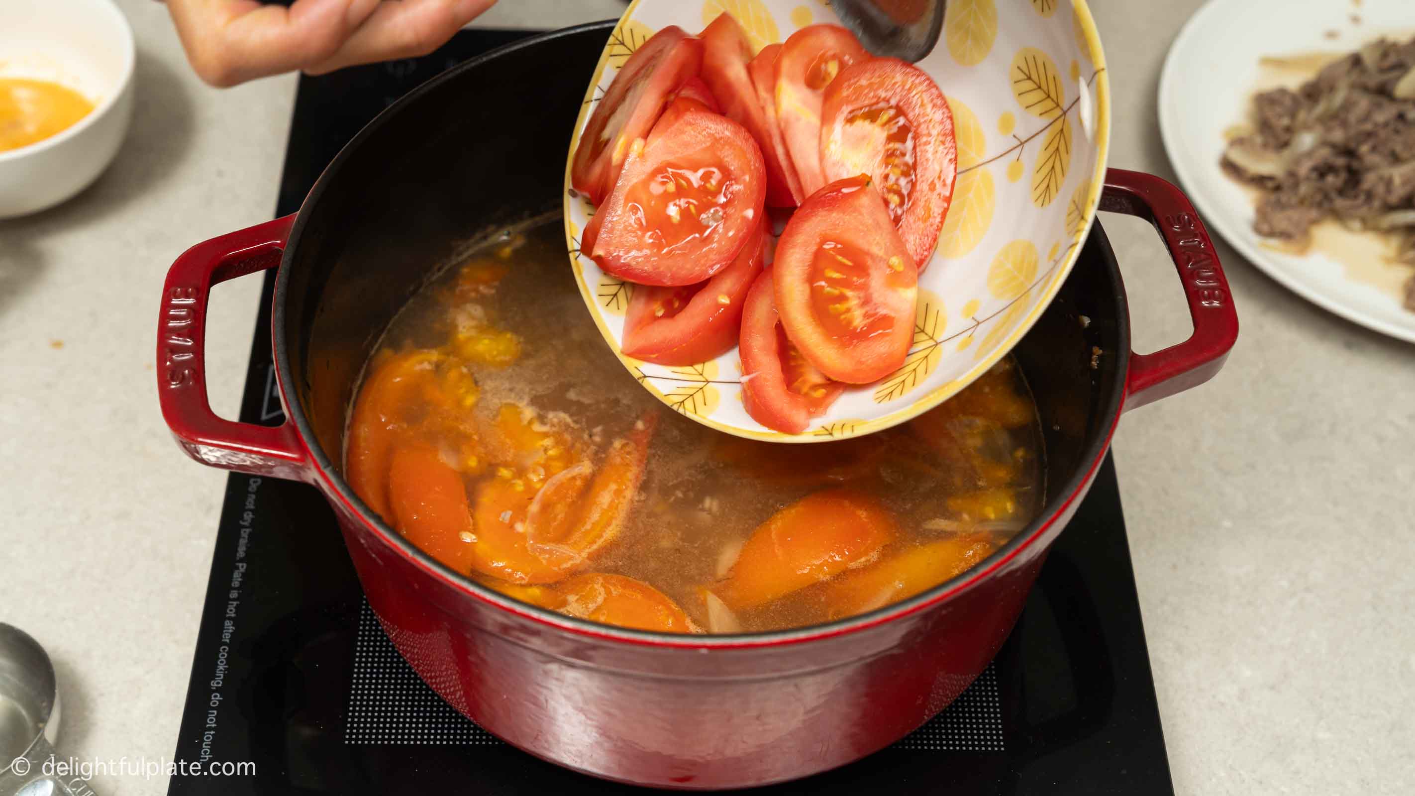adding tomatoes from a plate to the soup pot.