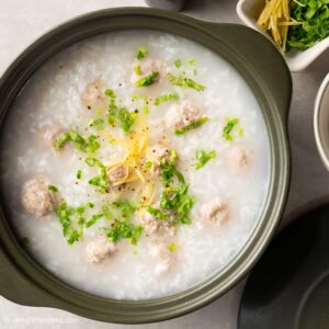 a bowl of congee with pork meatballs and toppings.