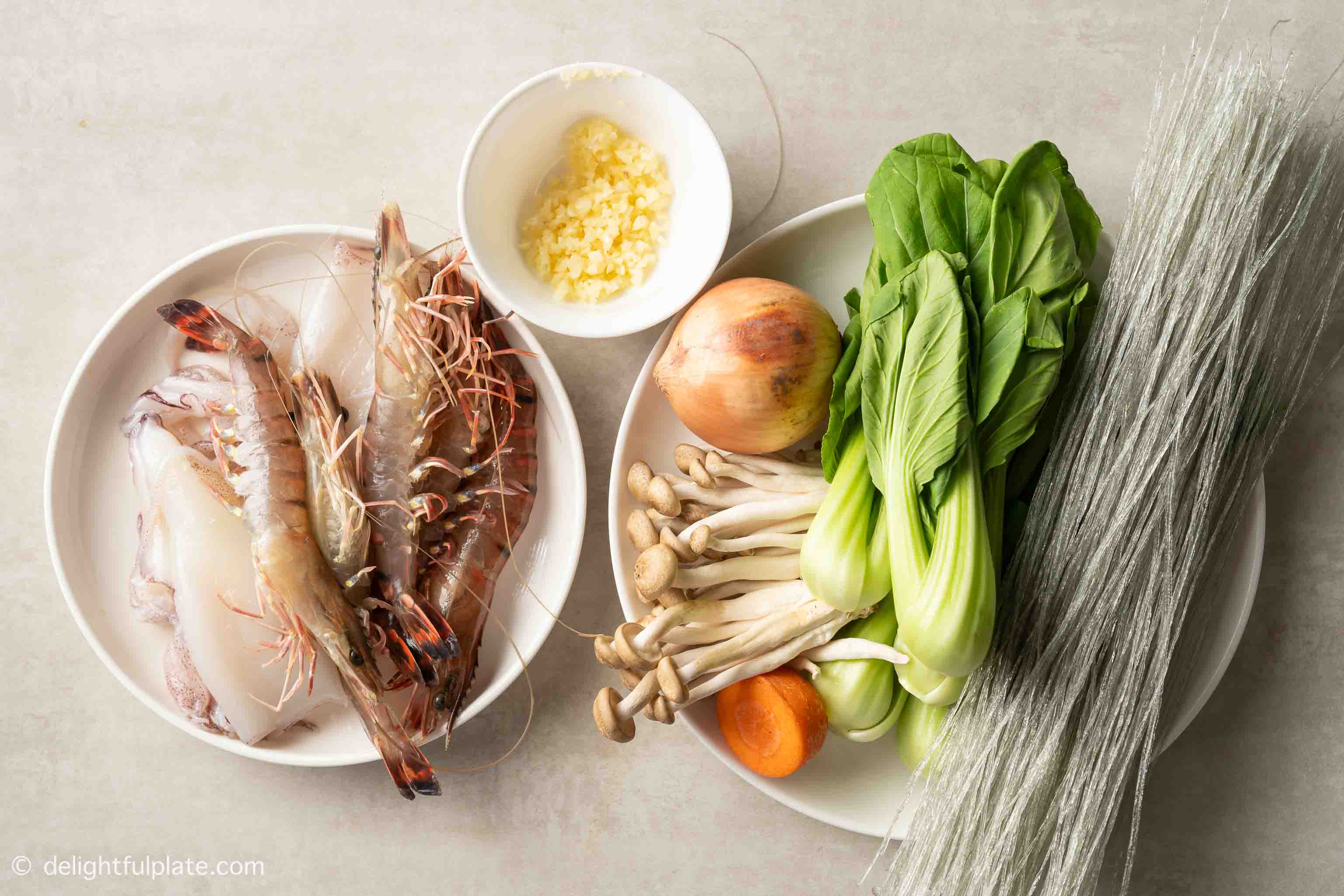 plates containing glass noodles, seafood and vegetables for the recipe.