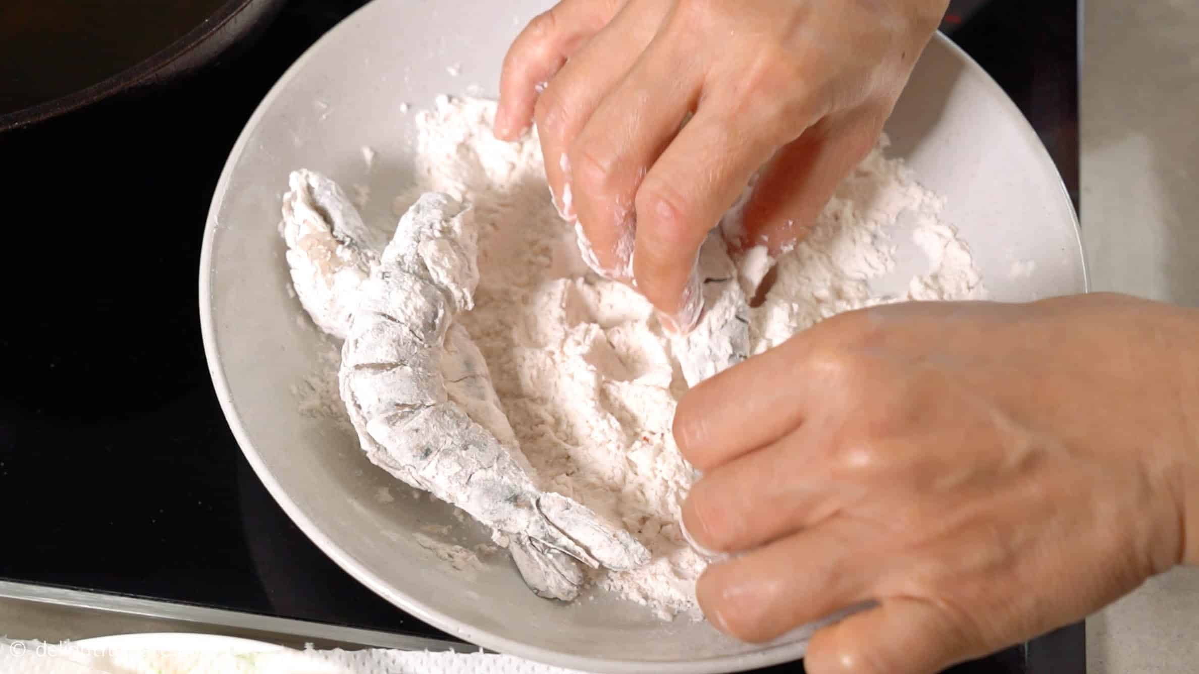 Coating shrimp with the flour mixture in a shallow plate.