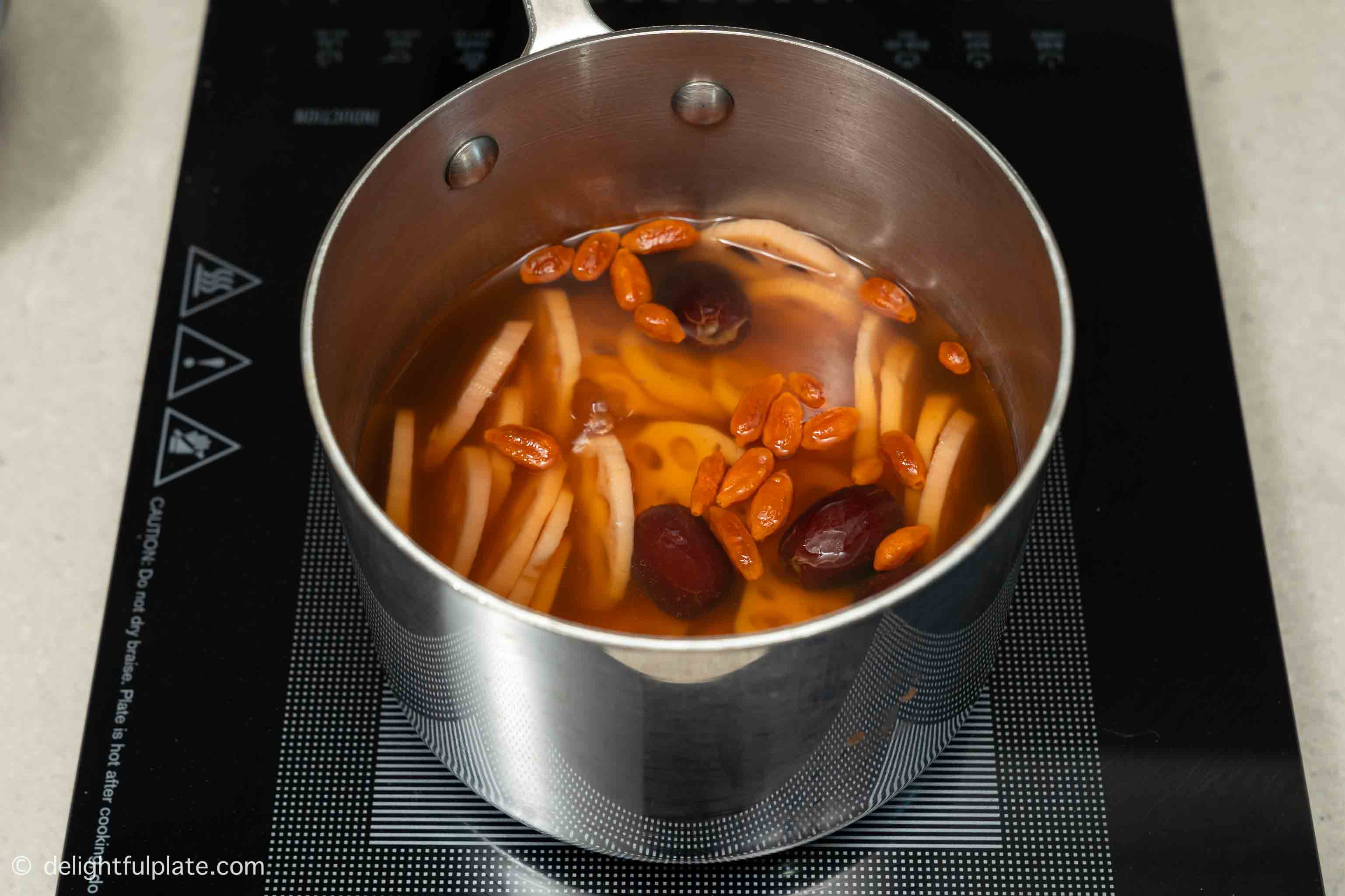 the pot of lotus root soup with goji berries and red dates on the cooktop.