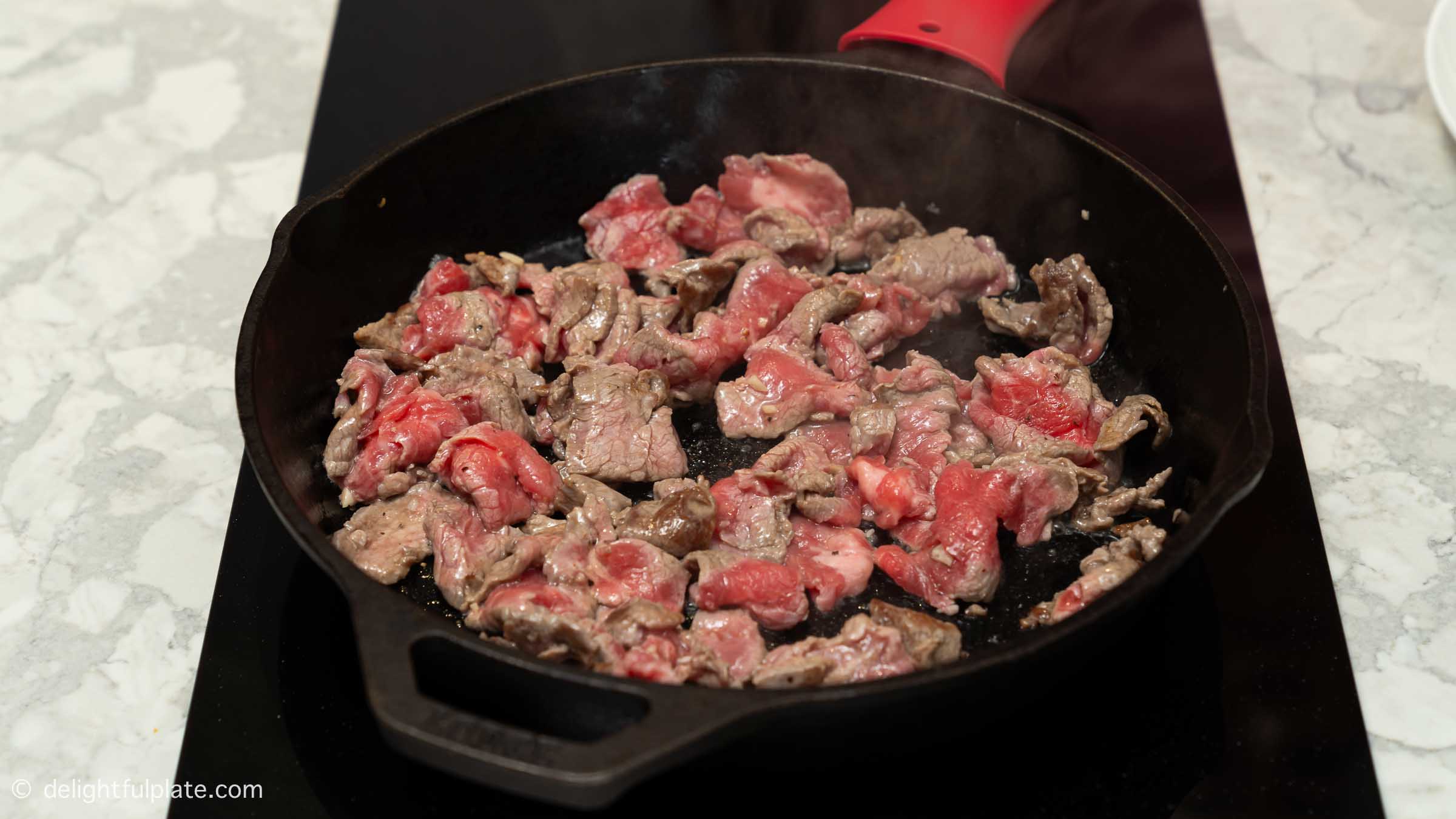 beef slices being stir-fried in a cast iron pan.