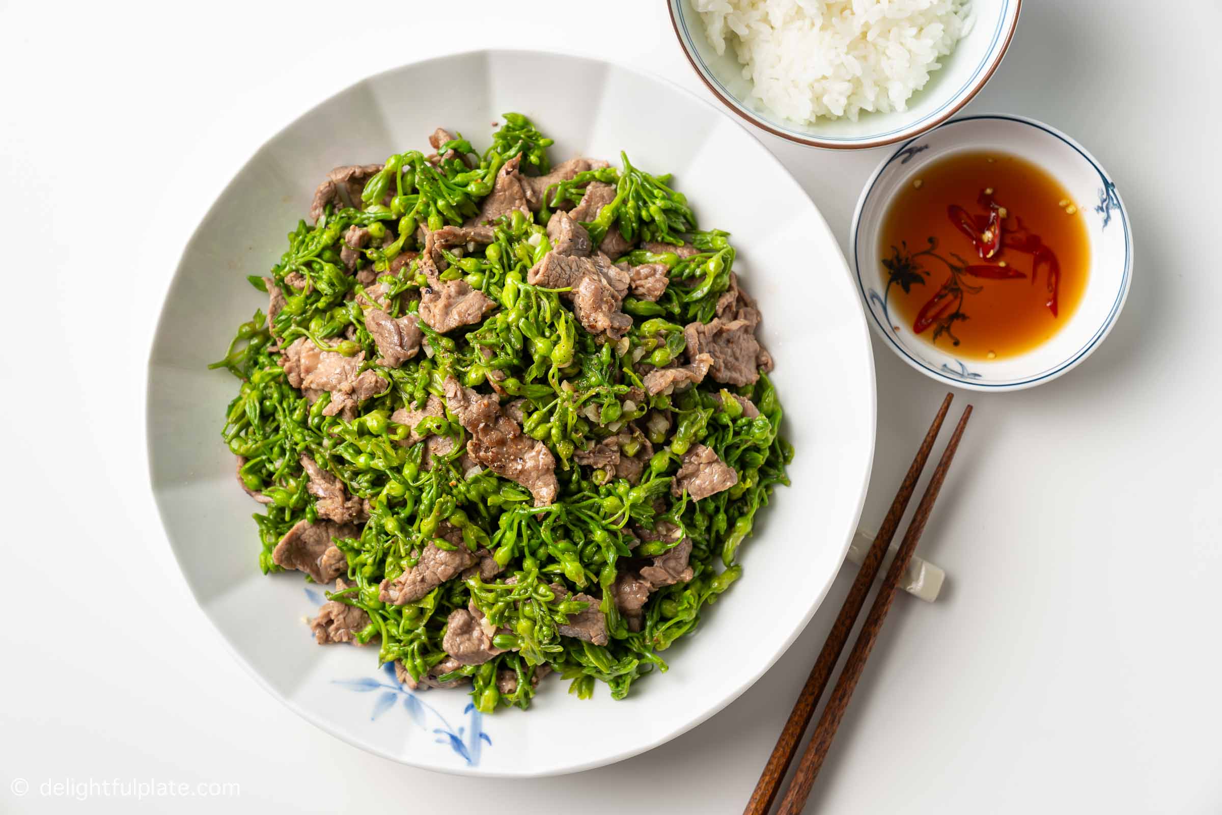 a plate of Vietnamese beef stir-fry with Tonkin flowers, served with a bowl of rice and a small plate of fish sauce on the side.