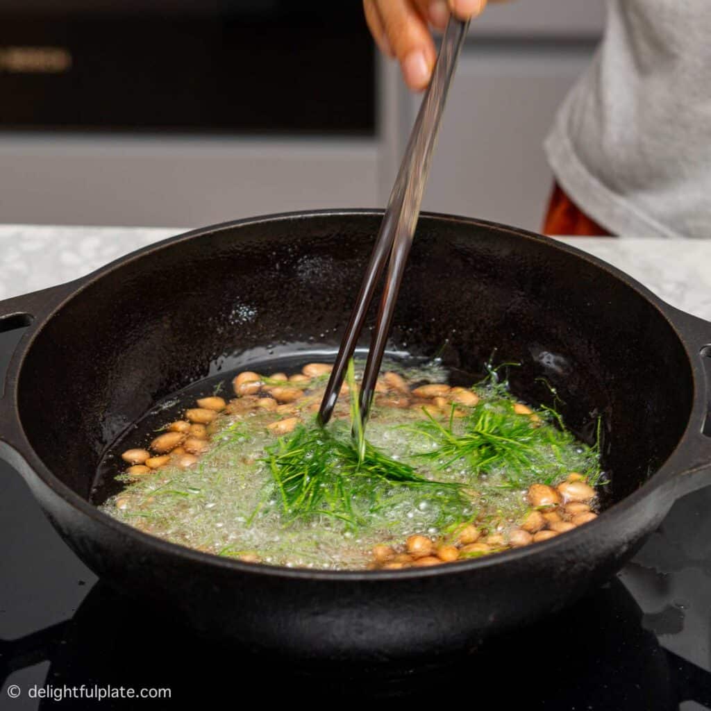 adding kaffir lime leaves to the fried peanuts in the wok.