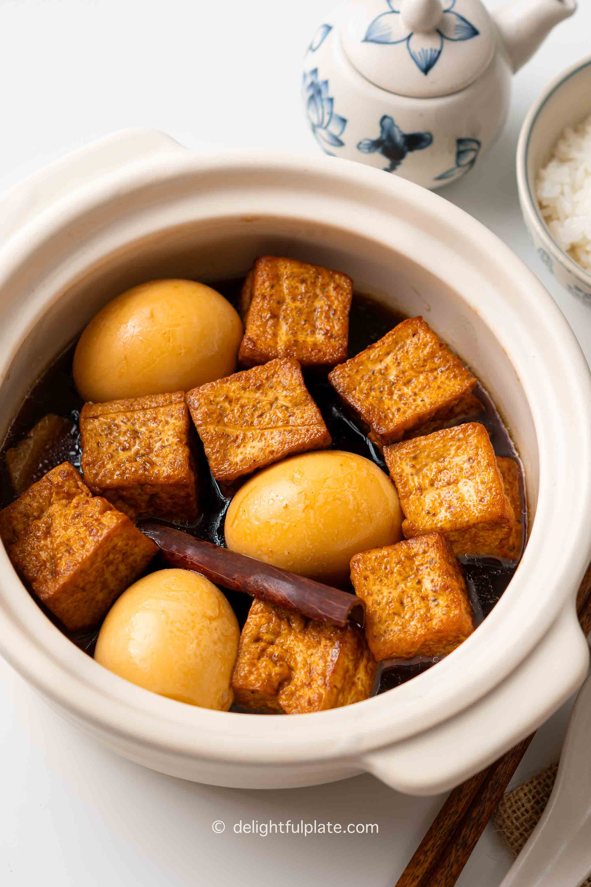 a bowl of braised tofu and eggs with soy sauce, served with rice on the side.