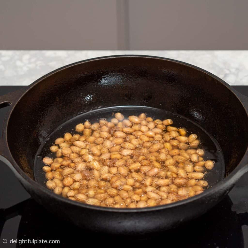 peanuts being fried in oil in a cast iron wok.
