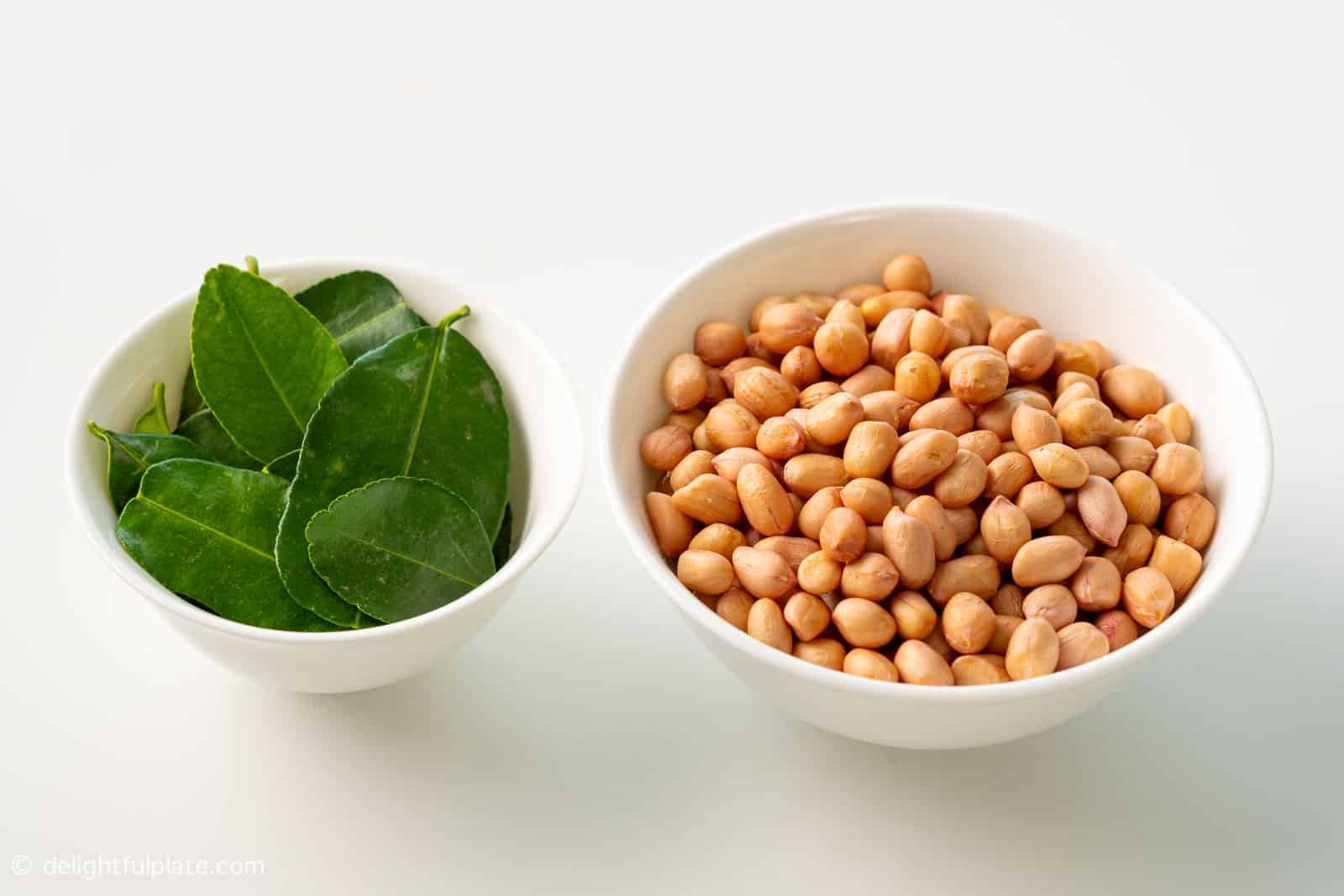 a bowl of raw peanuts and a bowl of kaffir lime leaves.