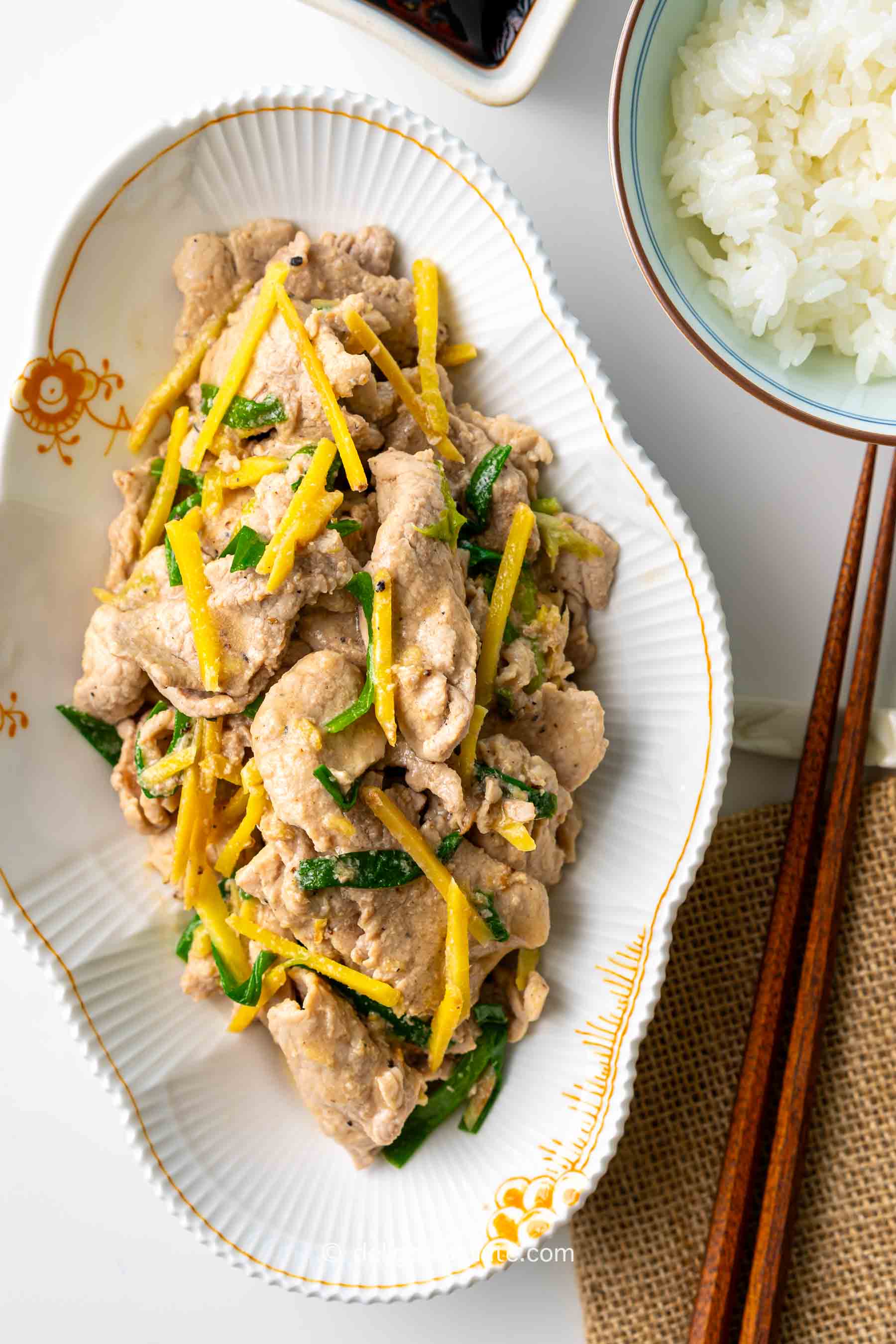 a plate of Vietnamese scallion ginger pork stir-fry (thit rim), served with a bowl of rice.