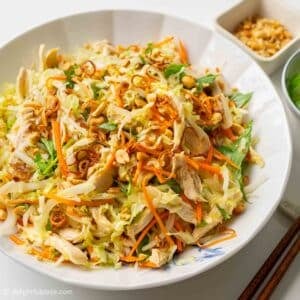 a plate of Vietnamese cabbage chicken salad with bowls of herbs and roasted peanuts on the side.