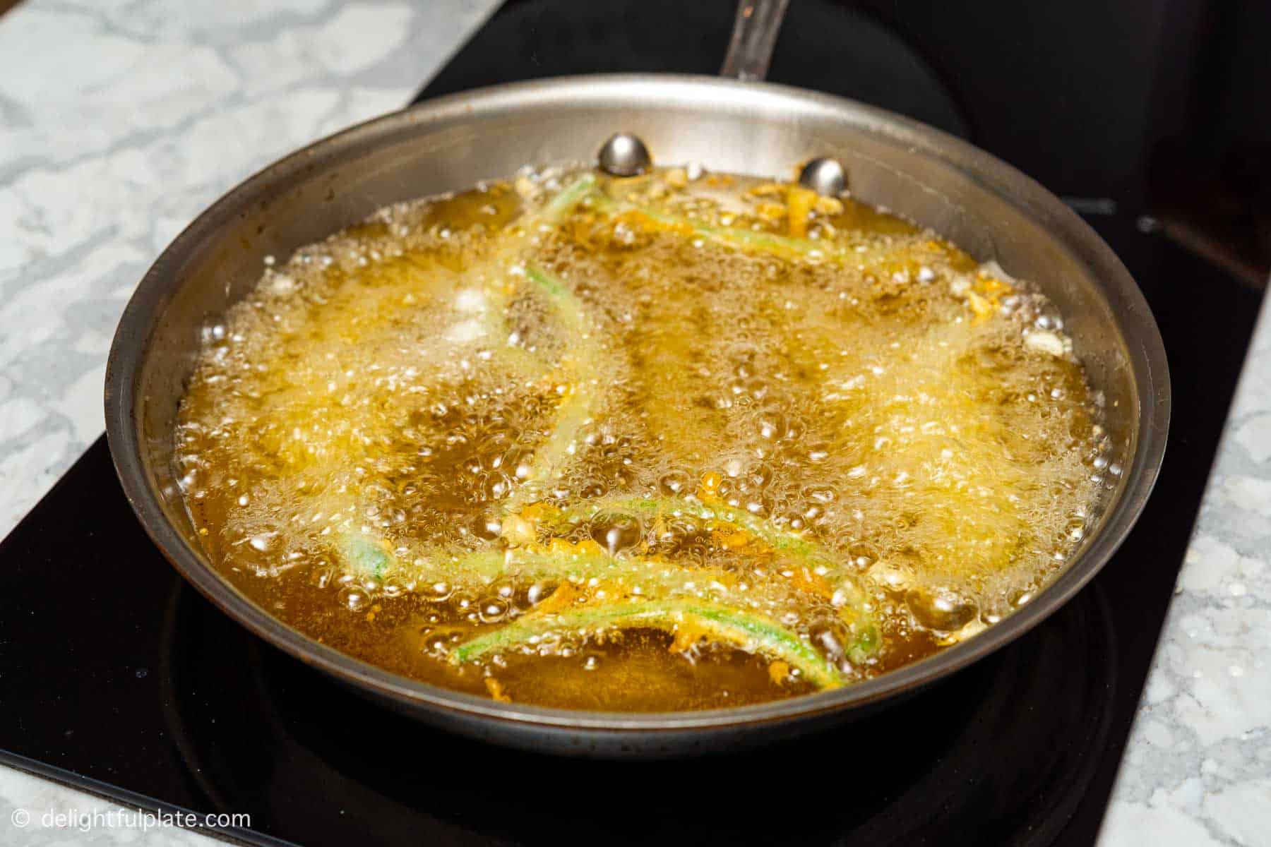 green beans being deep-fried in a stainless steel fry pan.