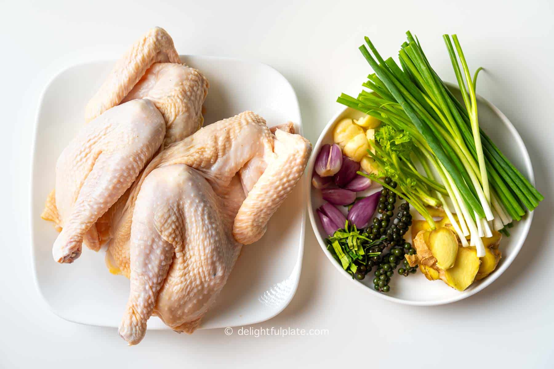 a plate with a whole raw chicken and a plate with aromatics for the recipe.