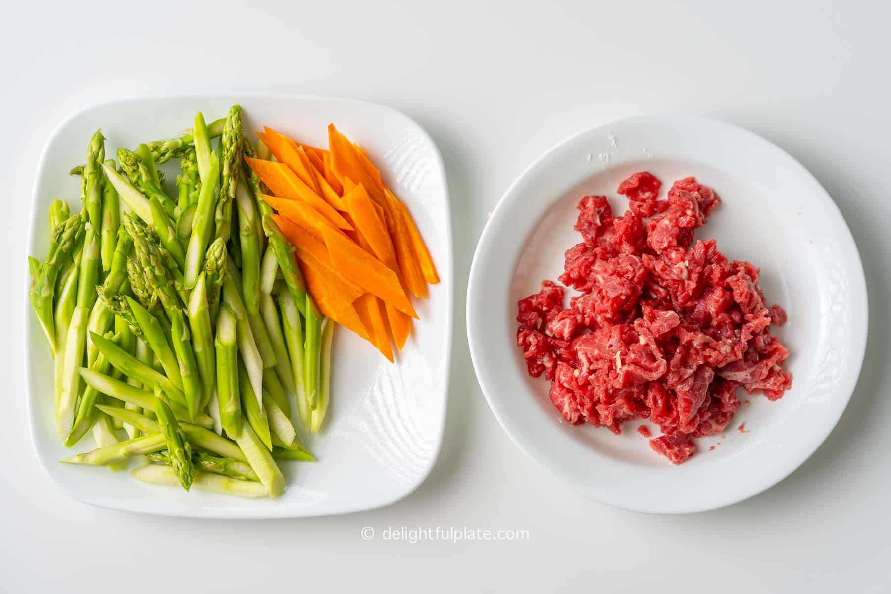 plates containing ingredients for stir-fried asparagus and beef.
