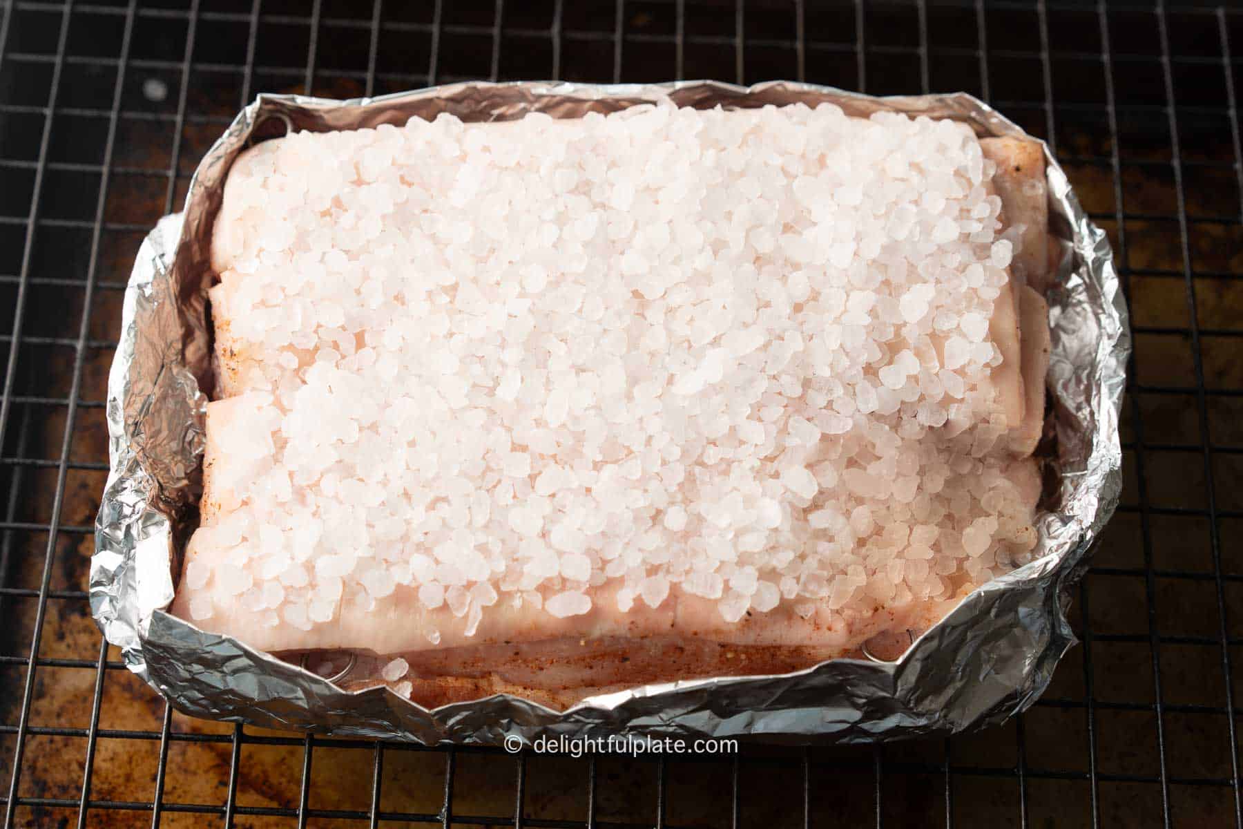 a slab of pork belly covered with coarse salt before roasting.